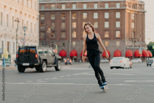 Active girl rollerblading on grey asphalt poses on rollers dressed in active wear drives fast leads healty lifestyle enjoys favorite hobby. Sport recreation roller skating summer time concept