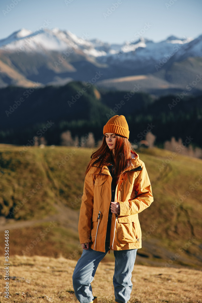 Woman fall stands a smile travels to the mountains in nature on a hike and happiness in a yellow raincoat against the snowy mountains in the sunset, freedom of life style