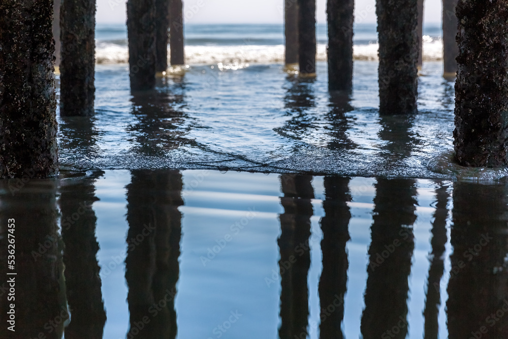 Selective focus on a gentle wave under the pier at Old Orchard Beach, Maine, USA. The pillars are reflected in the calm waters on a summer day