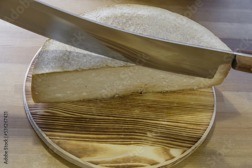 A man cuts a head of cheese with a large knife. photo