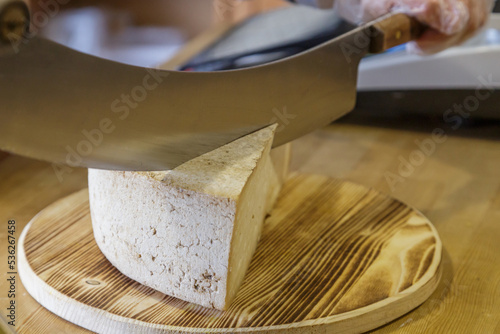 A man cuts a head of cheese with a large knife. photo