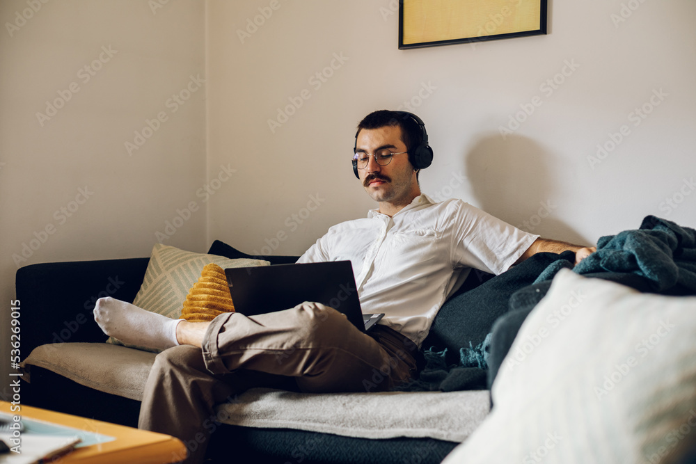 Man with a mustache working on laptop at home and using headphones Man with a mustache working on laptop at home and using headphones