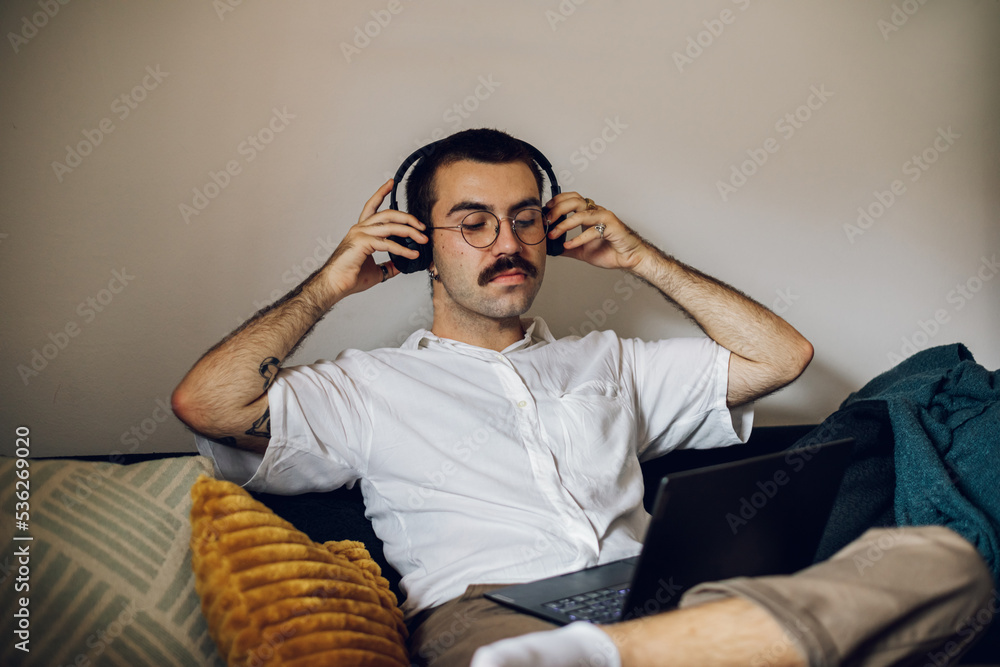 Obraz premium Man with a mustache working on laptop at home and using headphones