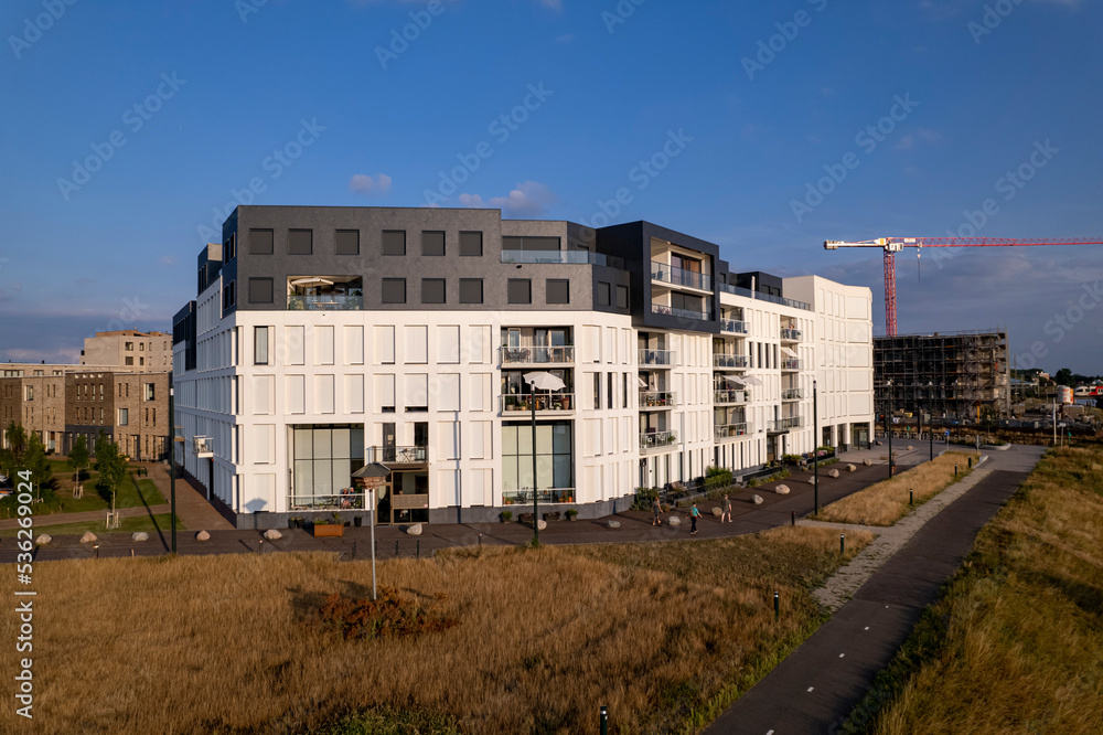 White exterior facade of newly build luxury apartment building in Hanseatic city with floodplains in the foreground and construction crane rising above