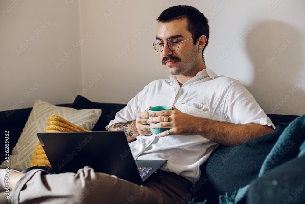 Man with a mustache drinking coffee and working on laptop at home Man with a mustache drinking coffee and working on laptop at home