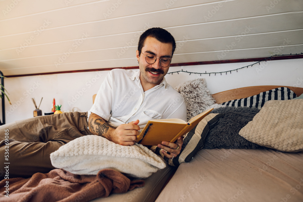 Fashionable hipster man with mustache reading a book while at home.