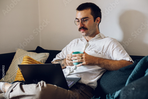 Man with a mustache drinking coffee and working on laptop at home