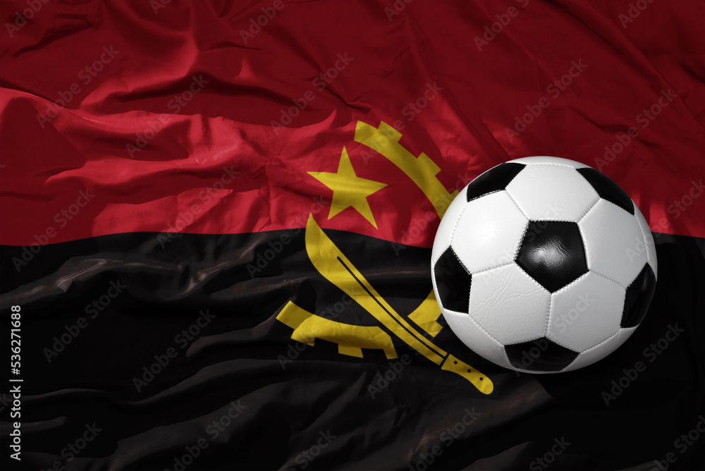 Naklejka premium vintage football ball on the waveing national flag of angola background. 3D illustration