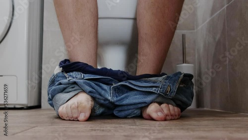 A man sits on the toilet in the toilet and clenches his toes during a bowel movement. Cognitive problems with bowel movements, constipation, close-up.