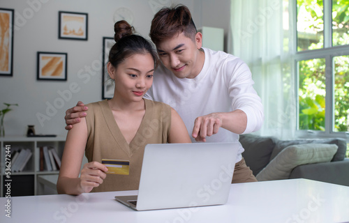 Young Asian couple holding credit card and using laptop computer. Happy man and woman working at home. Online shopping, e-commerce, internet banking, spending money, working from home concept