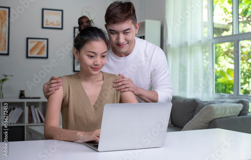 Happy young Asian couple communicating online on laptop. Loving Woman and Man embracing watching movie webinar on laptop.