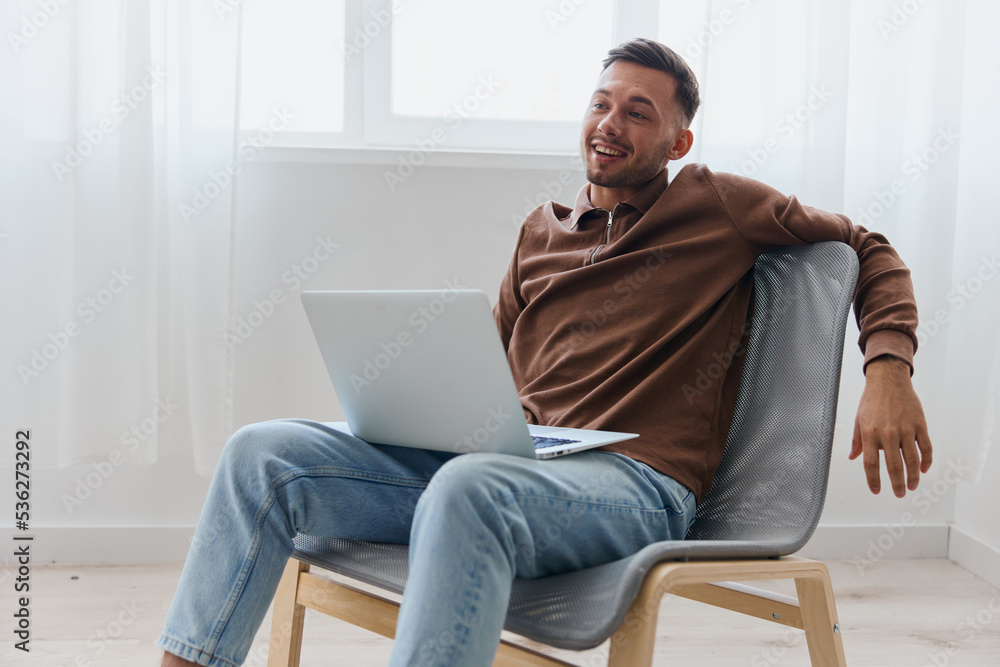 Cheerful successful happy young man guy leans back in chair rejoices at end of working day smiling looks aside at home. Remote Job, Distance Work and Career concept. Copy space