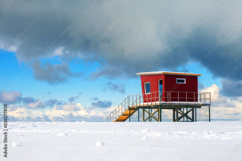 Red lifeguard tower or rescue tower on the snow covered beach, beautiful cloudy sky background Red lifeguard tower or rescue tower on the snow covered beach, beautiful cloudy sky background