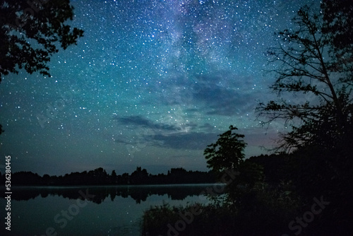 The starry sky over the forest lake. The Milky Way stretches across the sky  the stars are reflected in the water. enchanted lake shooting with a long shutter speed the effect of the movement of stars