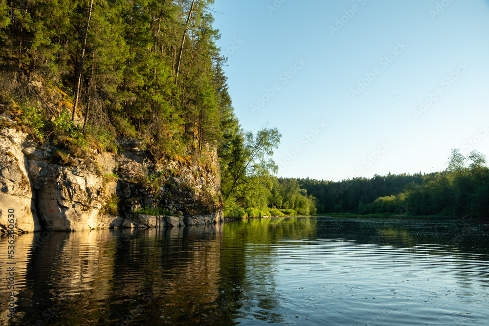 View of the river and a beautiful cliff illuminated by the sun during rafting on the river in summer. Amazing rocks are reflected in the water. Perfect river landscape