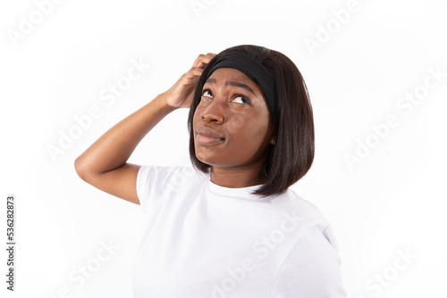 Portrait of forgetful young woman scratching head. African American lady wearing white T-shirt and headband looking away and wondering against white background. Forgetfullness concept photo