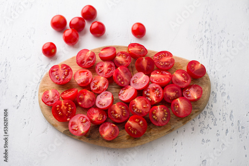 Wooden board with sliced cherry tomatoes on a light blue background, top view. Cooking delicious homemade food