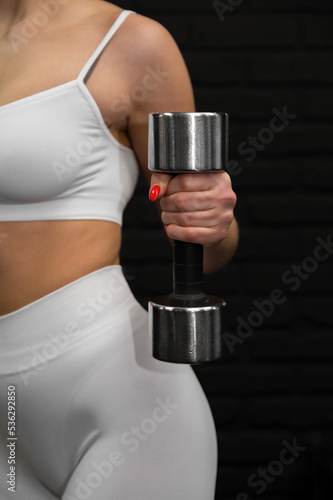Slim sporty girl stands front taned body in white underwear close-up shot keeps dumbbell weight in her hand with the black background text space to the right