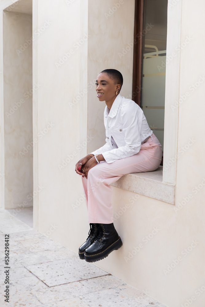 Short haired african american woman smiling while sitting on windowsill of building outdoors in Treviso.