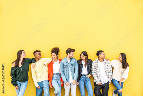 Diverse community of young people smiling together on a yellow wall background - Multiracial college students having fun laughing outside - Youth culture concept