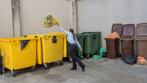 professional woman waitress throwing the yellow rubbish bag into the yellow waste bins, for plastic recycling. place with recycling bins, coloured waste bins, 