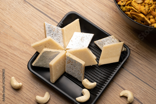 Kaju Katli is a traditional Indian Diamond shaped sweet or Mithai made using cashew paste, sugar, and mava or Khoya. served in a wooden plate over dark background. cashew barfi. photo