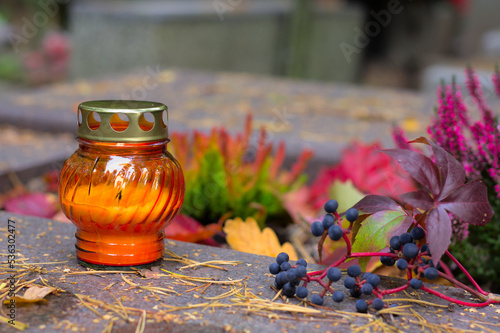 Fotografie An orange candle on a grave in a cemetery on an autumn day