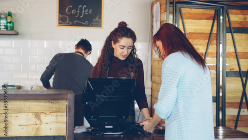 Fotografie Attractive woman talkative cashier is accepting contactless payments with mobile