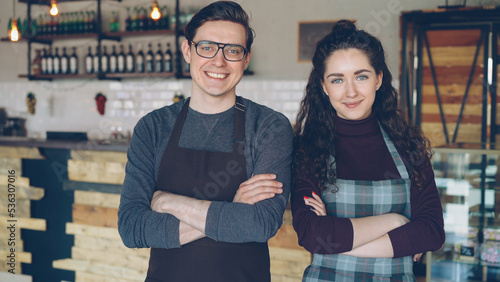 Portrait of two young coffee house owners attractive young people standing inside coffee-shop, smiling and looking at camera. Successful start-up and beautiful people concept.