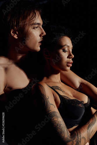 side view of tattooed woman with sexy breast near shirtless man isolated on black.