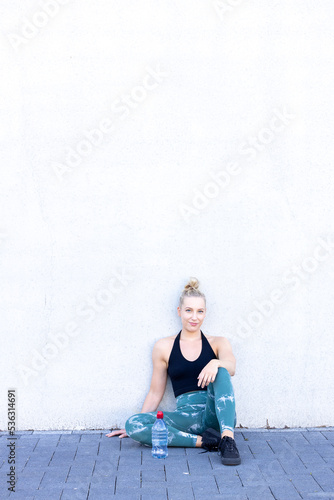 Sport and lifestyle concept, woman resting after doing sports outdoors. Attractive young blonde Caucasian woman relax after workout with happiness and joy, and a water bottle Full length shot of an