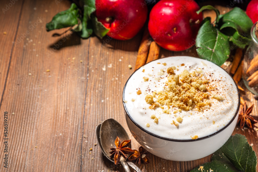 Bowl of homemade apple pie yogurt ready for breakfast, with tart crumble topping. On wooden background with red autumn apples and spices, copy space Bowl of homemade apple pie yogurt ready for breakfast, with tart crumble topping. On wooden background with red autumn apples and spices, copy space