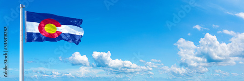 Colorado - state of USA, flag waving on a blue sky in beautiful clouds - Horizontal banner 