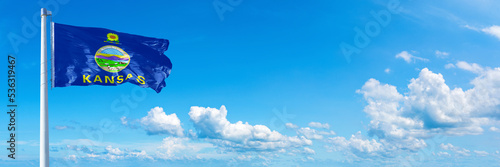 Kansas - state of USA, flag waving on a blue sky in beautiful clouds - Horizontal banner 