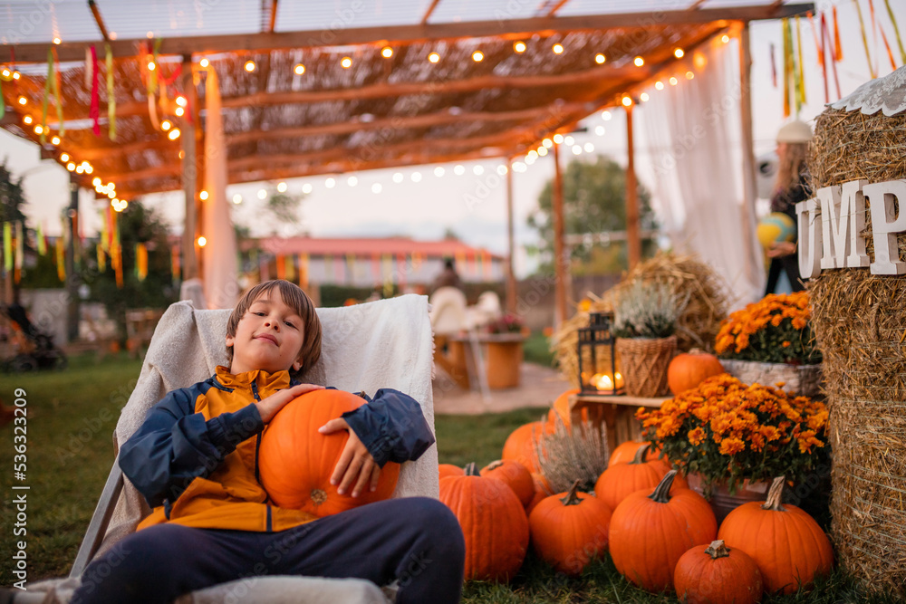 Naklejka premium Cute happy toddler boy in the pampking farm outdoor before Thanksgiving day. Pumpkin harvest in autumn. Helloween concept