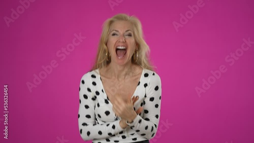 Excited jubilant overjoyed happy blonde woman 50s wears polka dot shirt doing winner gesture celebrate clenching fists say yes isolated on solid pink background studio portrait