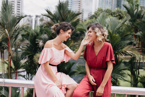 Wonderful brunette female model laughing with best friend on city background. Stunning ladies spending time in beautiful place with palm trees.