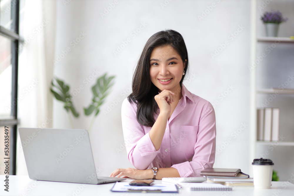 Portrait of a charming Asian business woman smiling happily working on a laptop in the home office. Portrait of a charming Asian business woman smiling happily working on a laptop in the home office.