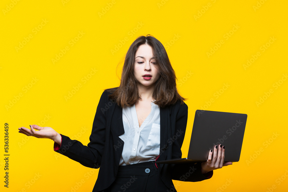 Portrait of a young woman in a business suit with a laptop on a yellow background. Portrait of a young woman in a business suit with a laptop on a yellow background.
