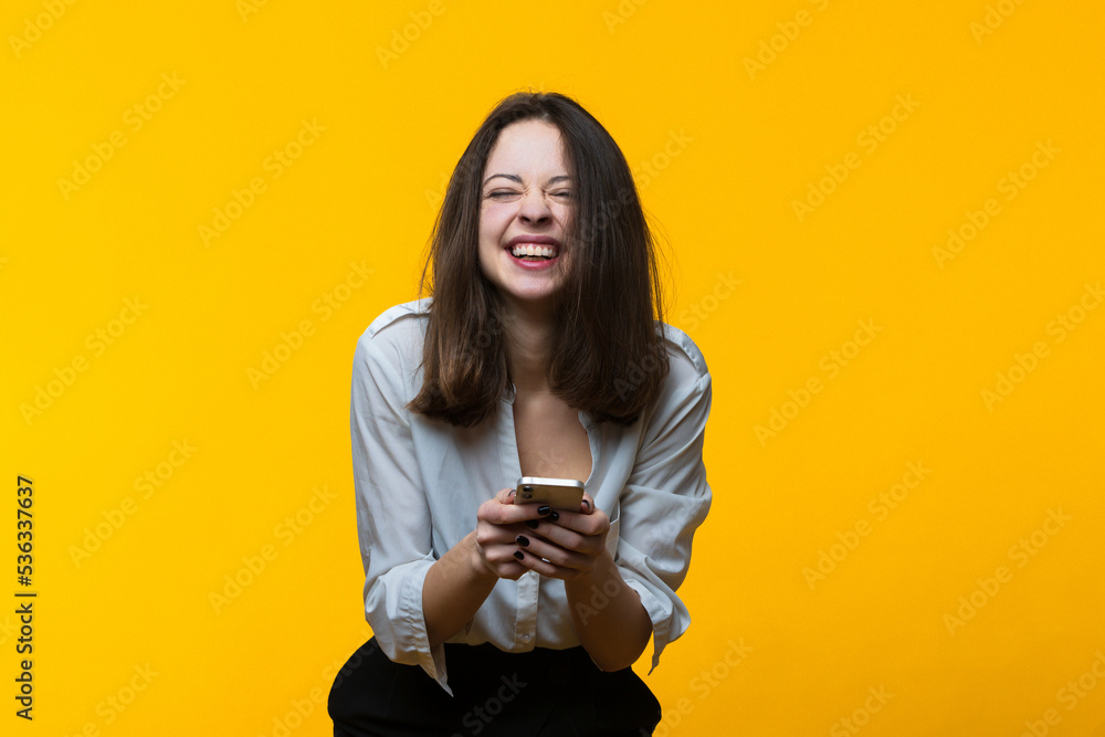 A happy young woman with a phone in her hands on a yellow background. A happy young woman with a phone in her hands on a yellow background.