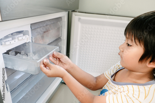 Little Asian kid making some ice using the ice maker in the refrigerator photo