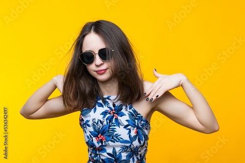 Attractive young woman in a dress and sunglasses on a yellow background.