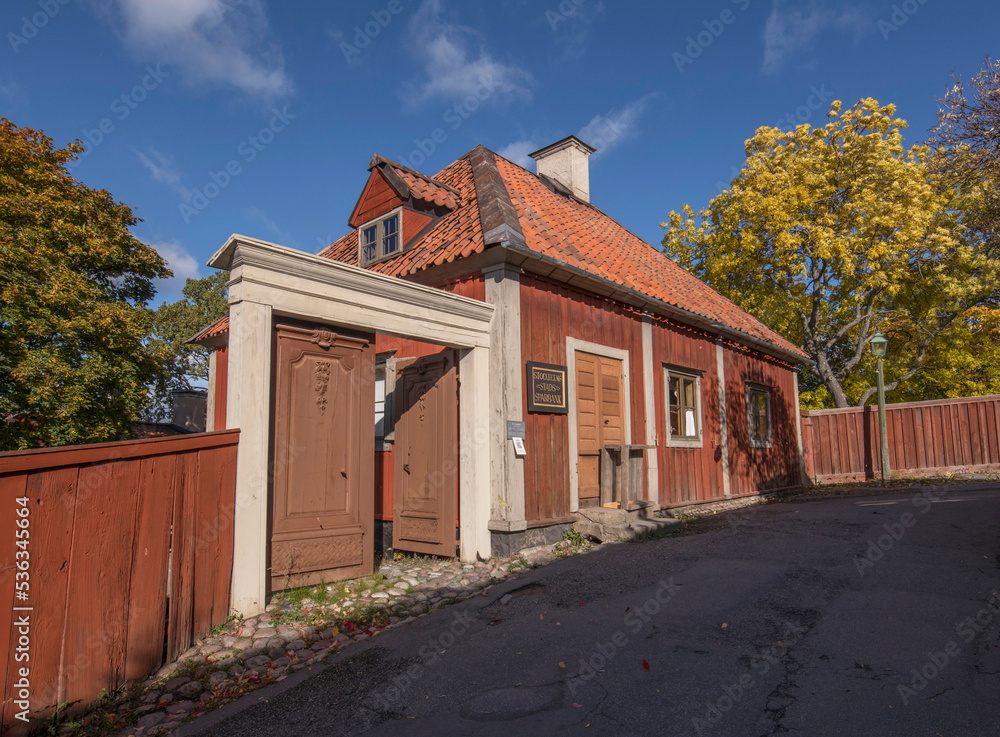 Old 1800s wood store house with dorm and chimney on a red tile roof a colorful sunny autumn day in Stockholm