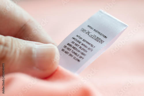 Hand hold and reading at white laundry care washing instructions clothes label on pink shirt