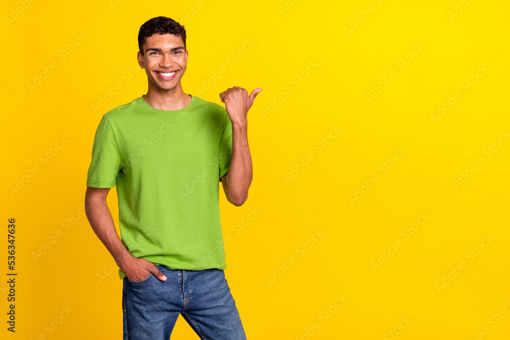Photo portrait of attracive young guy smiling finger point empty promo space dressed trendy green look isolated on yellow color background Photo portrait of attracive young guy smiling finger point empty promo space dressed trendy green look isolated on yellow color background