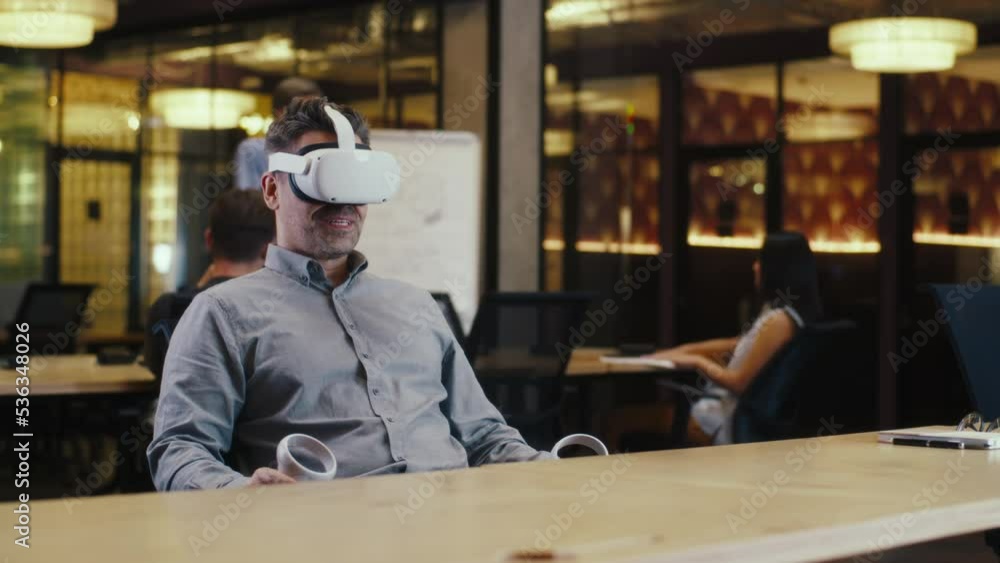 Man using VR headset and wireless controllers, speaking online with client, having video call, working in modern office of hi-tech company. Business virtual meeting. Cyberspace digital technology Man using VR headset and wireless controllers, speaking online with client, having video call, working in modern office of hi-tech company. Business virtual meeting. Cyberspace digital technology