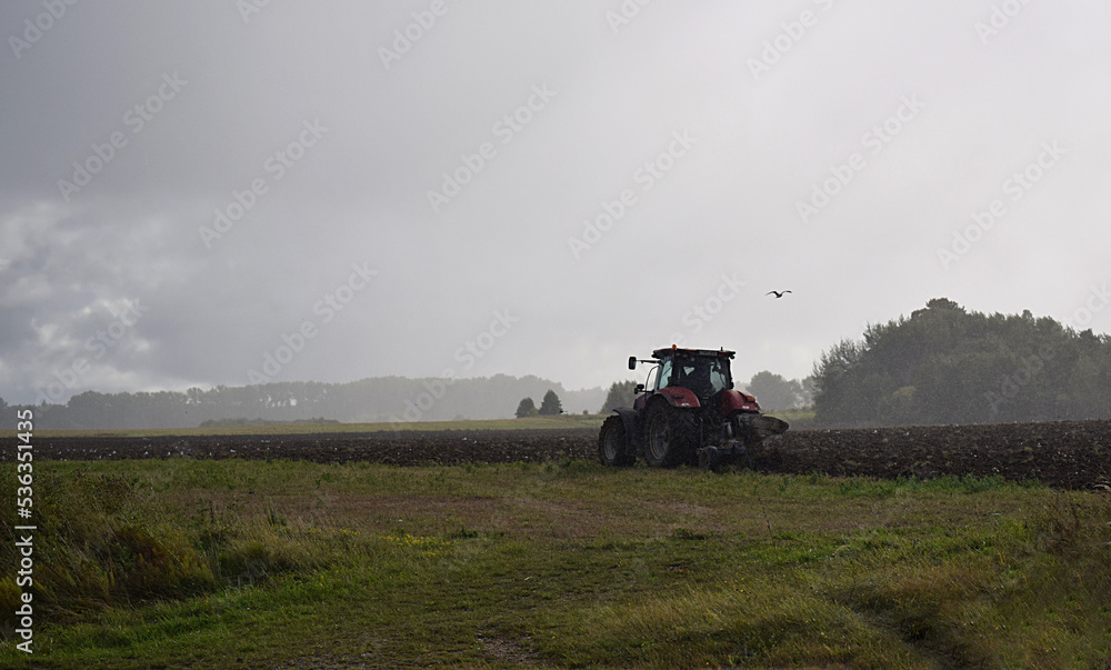 Fototapeta premium tractor with plow on field in bad weather