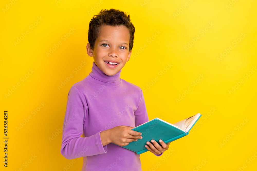 Photo of positive clever schoolchild hands hold opened book toothy smile isolated on yellow color background Photo of positive clever schoolchild hands hold opened book toothy smile isolated on yellow color background