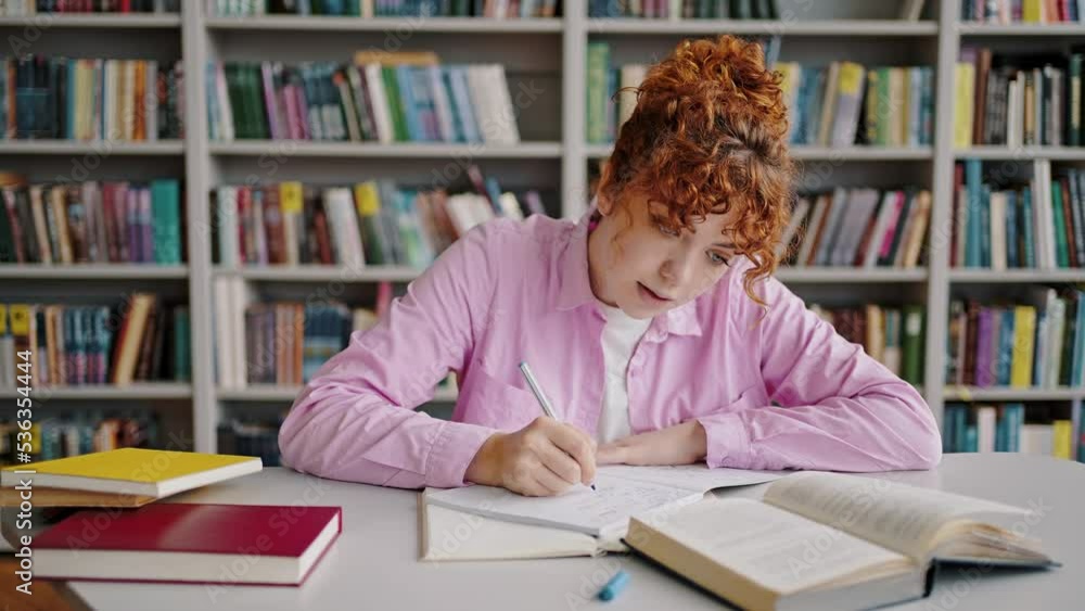 Redhead girl summarizes material from textbook in library Redhead girl summarizes material from textbook in library