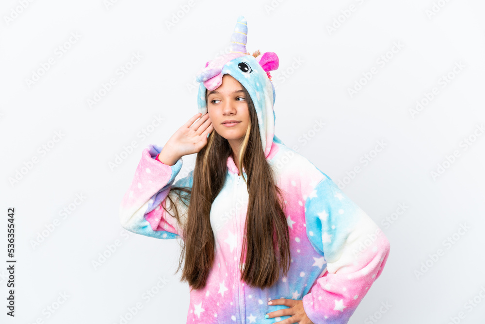 Little caucasian girl wearing unicorn pajama isolated on white background listening to something by putting hand on the ear Little caucasian girl wearing unicorn pajama isolated on white background listening to something by putting hand on the ear